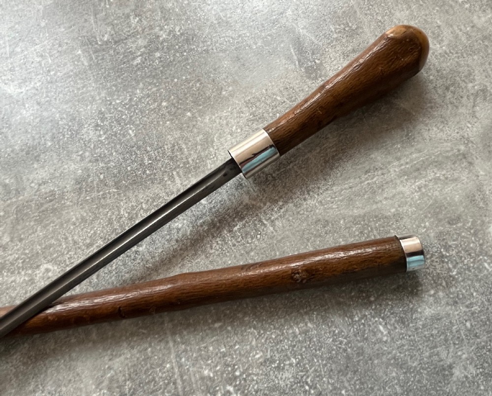 An antique chestnut wood sword stick shown unsheathed beside its shaft, featuring a root ball knob handle, silver collar mount, and long steel blade. View XI