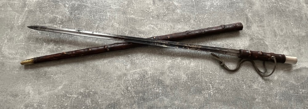 An antique sword stick with a dark brown leather-covered shaft, a silver knop top, and a partially drawn steel blade decorated with gold-toned etchings. View XII