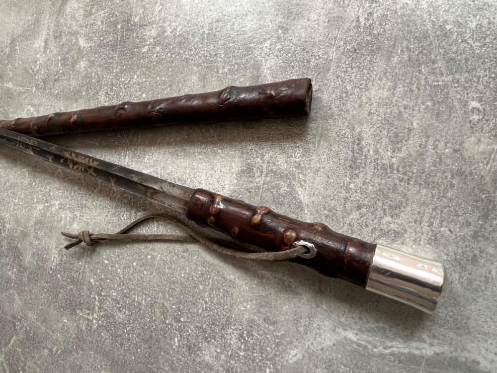 An antique sword stick with a dark brown leather-covered shaft, a silver knop top, and a partially drawn steel blade decorated with gold-toned etchings. View XIV