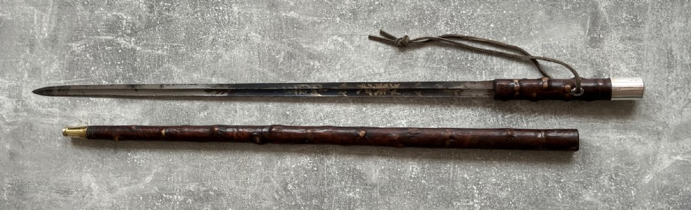 An antique sword stick with a dark brown leather-covered shaft, a silver knop top, and a partially drawn steel blade decorated with gold-toned etchings. View XV