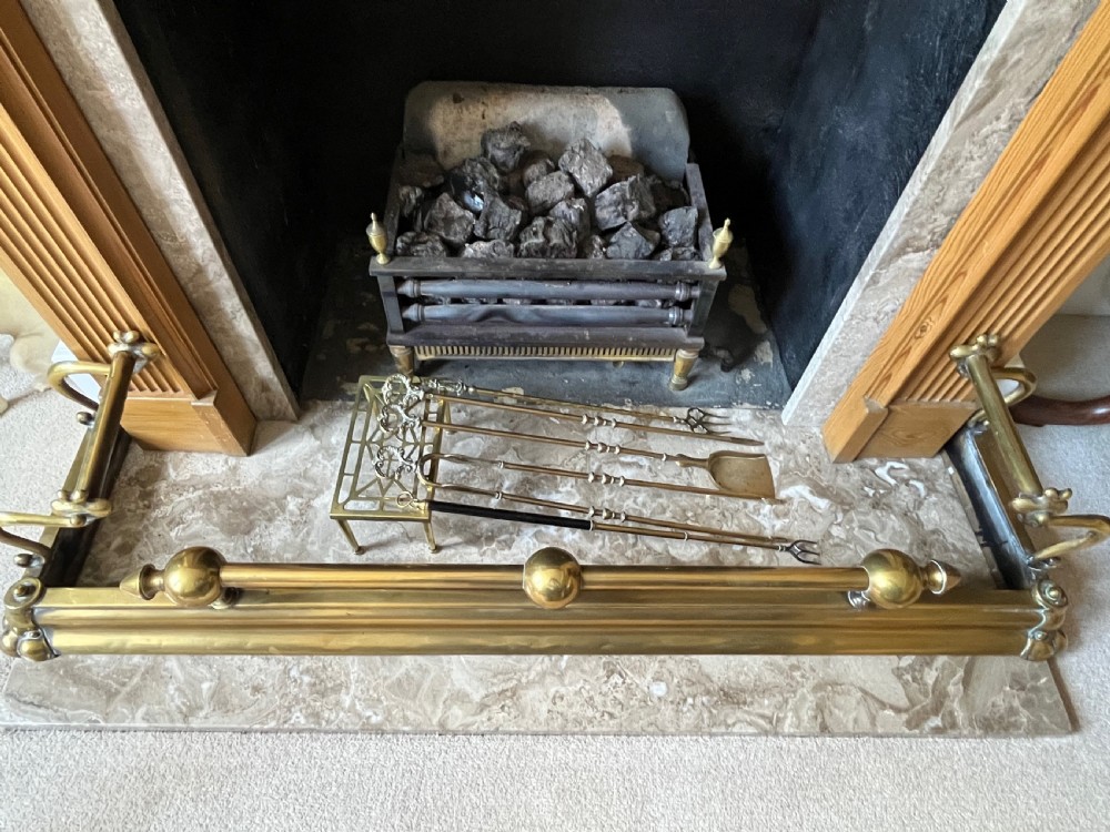 A low brass fire fender with rounded finials set around a hearth with matching brass companion tools on a small stand.