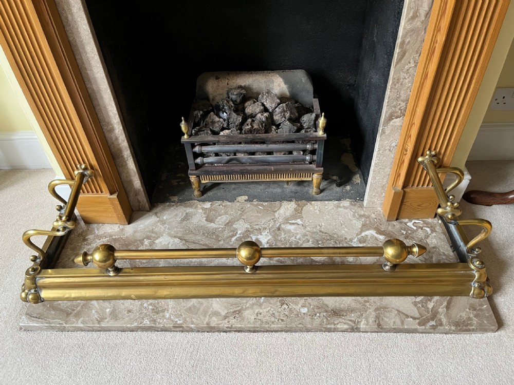 A low brass fire fender with rounded finials set around a hearth with matching brass companion tools on a small stand. View II