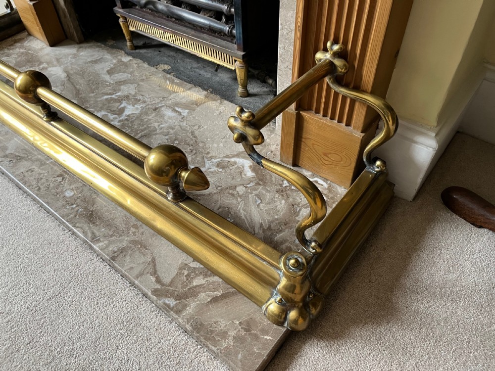 A low brass fire fender with rounded finials set around a hearth with matching brass companion tools on a small stand. View III