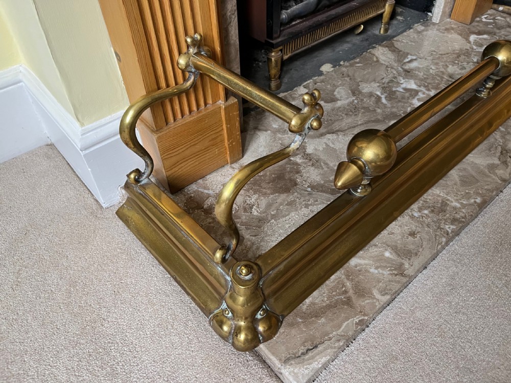 A low brass fire fender with rounded finials set around a hearth with matching brass companion tools on a small stand. View IV
