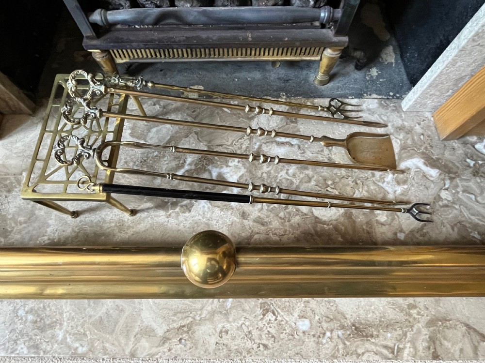 A low brass fire fender with rounded finials set around a hearth with matching brass companion tools on a small stand. View V