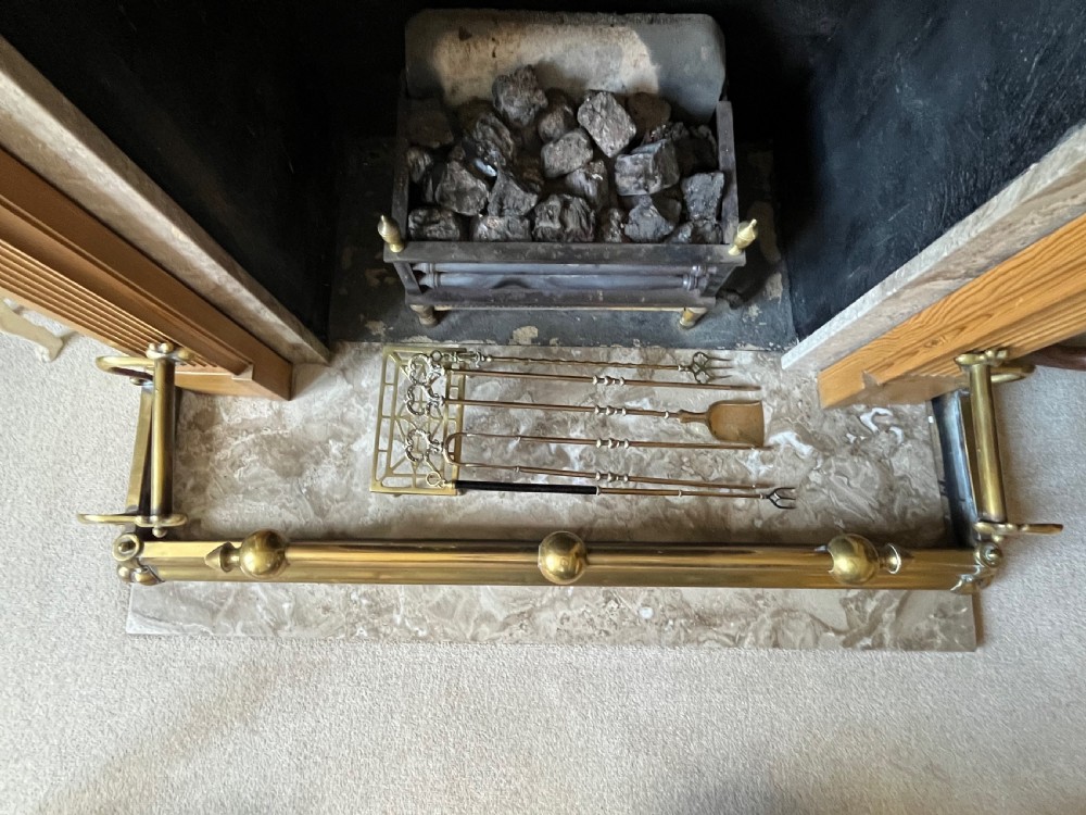 A low brass fire fender with rounded finials set around a hearth with matching brass companion tools on a small stand. View VI