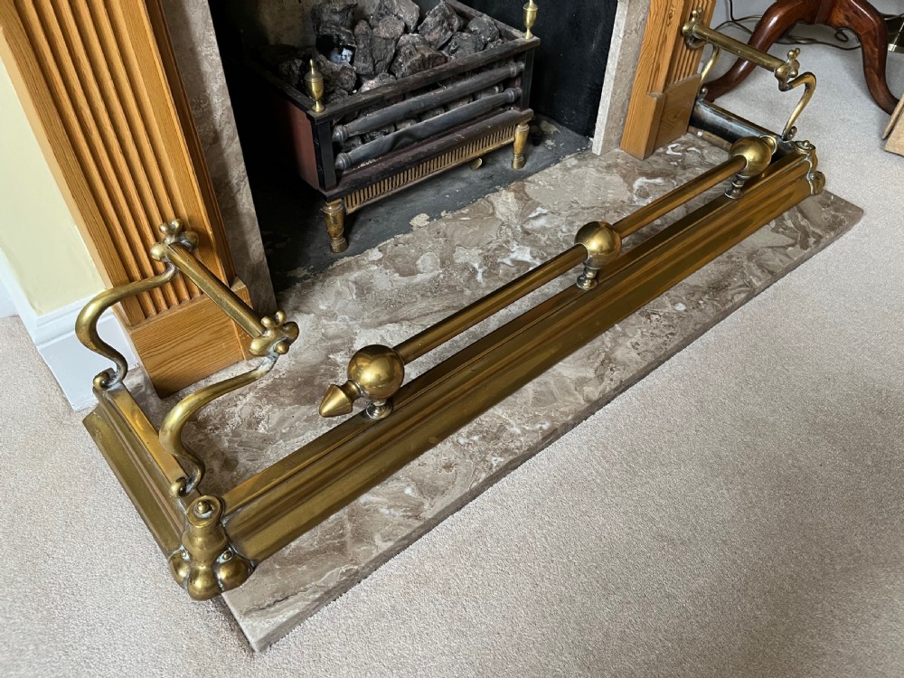 A low brass fire fender with rounded finials set around a hearth with matching brass companion tools on a small stand. View VII
