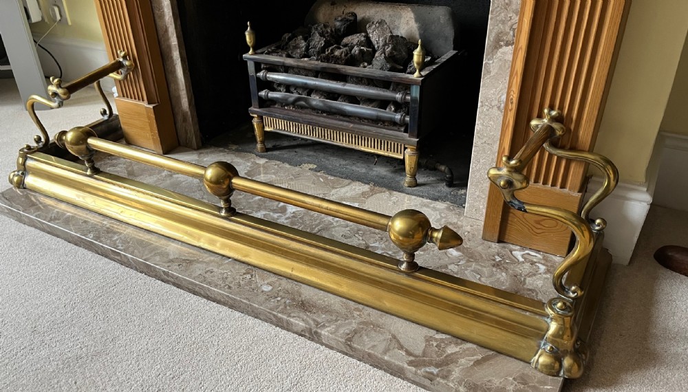 A low brass fire fender with rounded finials set around a hearth with matching brass companion tools on a small stand. View VIII