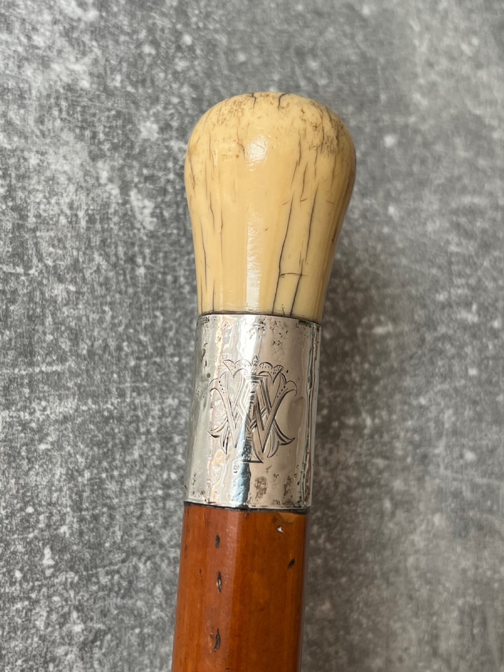 An antique Malacca sword stick shown unsheathed, featuring an etched steel blade, a polished wooden shaft, a silver collar, and a carved bone knop handle. View VI