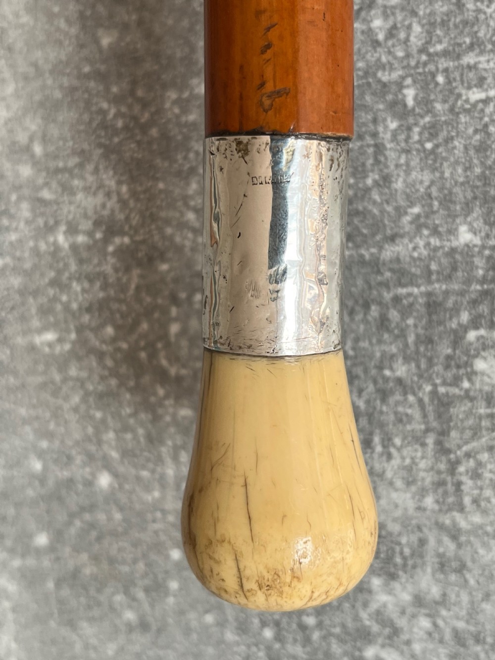 An antique Malacca sword stick shown unsheathed, featuring an etched steel blade, a polished wooden shaft, a silver collar, and a carved bone knop handle. View VII