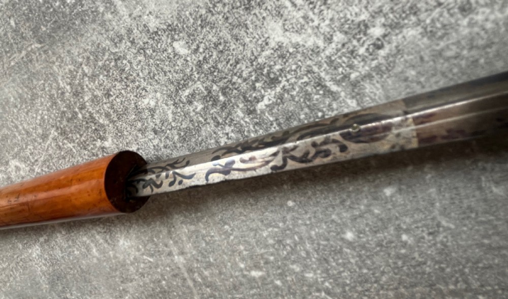 An antique Malacca sword stick shown unsheathed, featuring an etched steel blade, a polished wooden shaft, a silver collar, and a carved bone knop handle. View IX