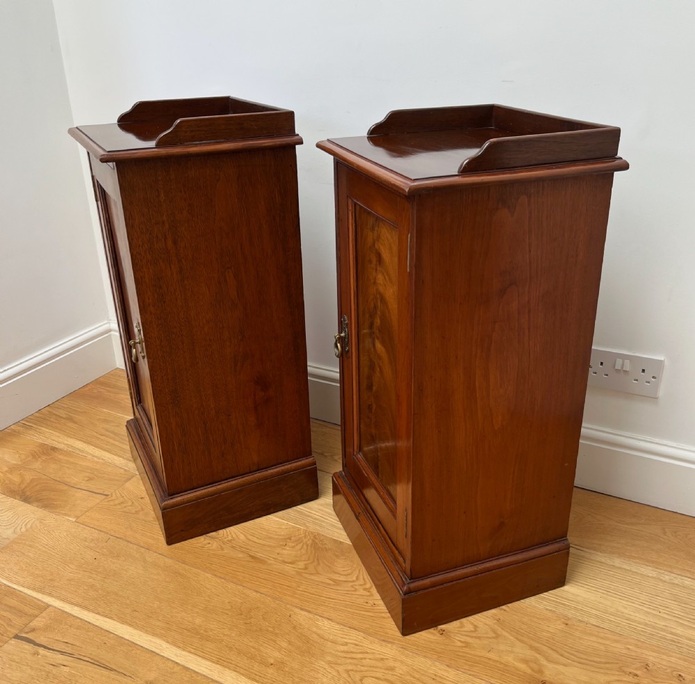 A pair of antique mahogany bedside cabinets featuring gallery tops, single panelled doors, brass drop handles, and solid plinth bases. View VI