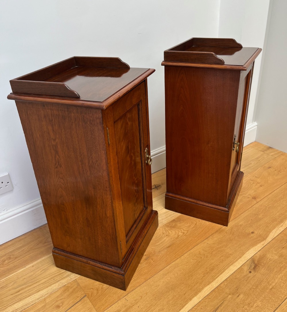 A pair of antique mahogany bedside cabinets featuring gallery tops, single panelled doors, brass drop handles, and solid plinth bases. View VII