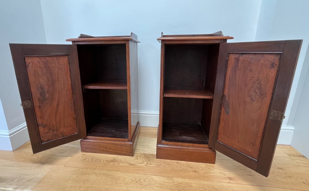 A pair of antique mahogany bedside cabinets featuring gallery tops, single panelled doors, brass drop handles, and solid plinth bases. View IX