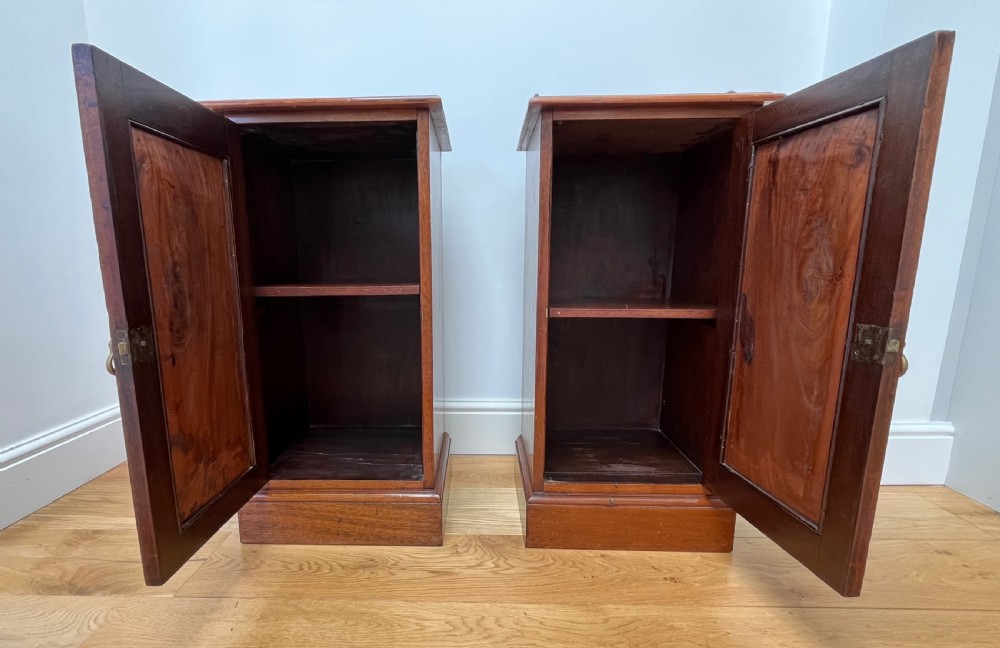 A pair of antique mahogany bedside cabinets featuring gallery tops, single panelled doors, brass drop handles, and solid plinth bases. View XII