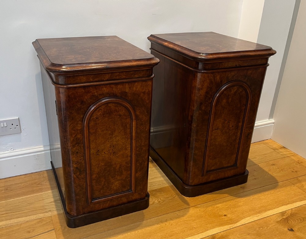 A matching pair of antique burr walnut bedside cabinets featuring single door cupboards with recessed arched panels and plinth bases.