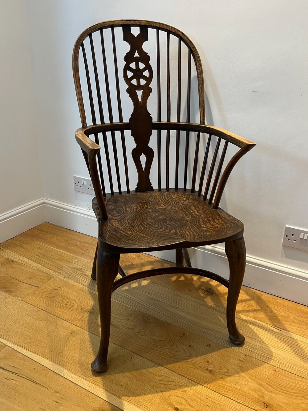 A dark brown wooden Windsor armchair featuring a high hoop back with a wheel-motif central splat, curved armrests, a contoured saddle seat, and front cabriole legs. View II