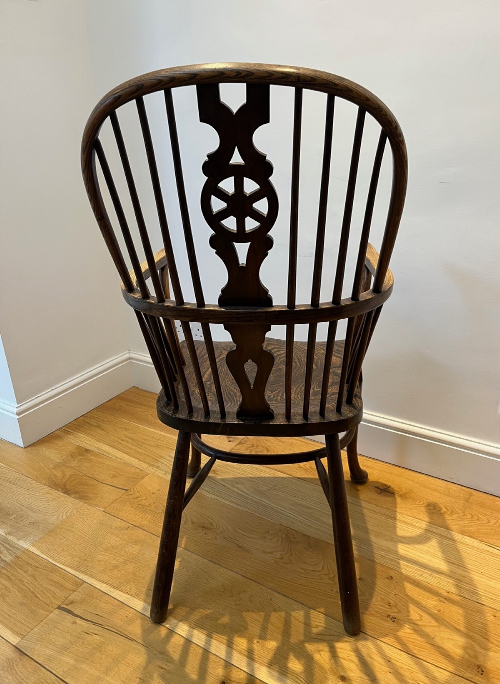 A dark brown wooden Windsor armchair featuring a high hoop back with a wheel-motif central splat, curved armrests, a contoured saddle seat, and front cabriole legs. View V