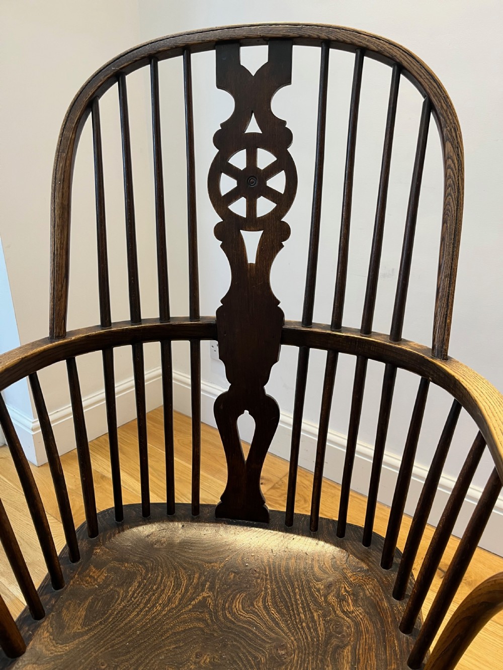 A dark brown wooden Windsor armchair featuring a high hoop back with a wheel-motif central splat, curved armrests, a contoured saddle seat, and front cabriole legs. View VII