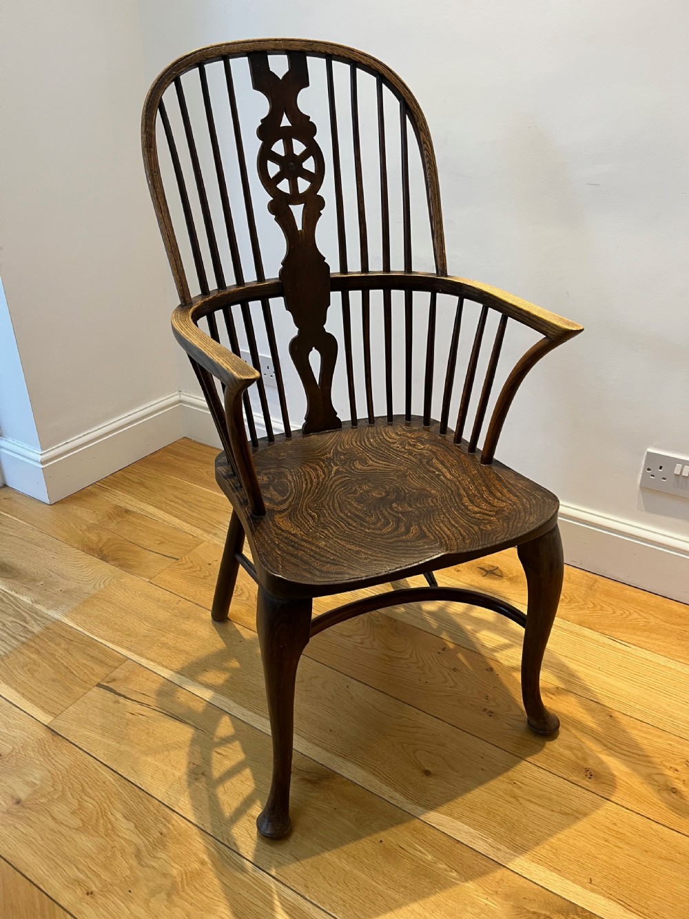 A dark brown wooden Windsor armchair featuring a high hoop back with a wheel-motif central splat, curved armrests, a contoured saddle seat, and front cabriole legs. View IX