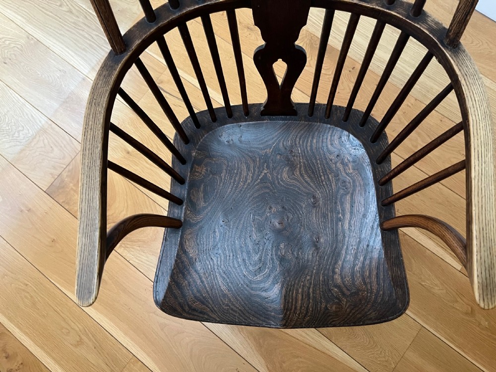 A dark brown wooden Windsor armchair featuring a high hoop back with a wheel-motif central splat, curved armrests, a contoured saddle seat, and front cabriole legs. View X