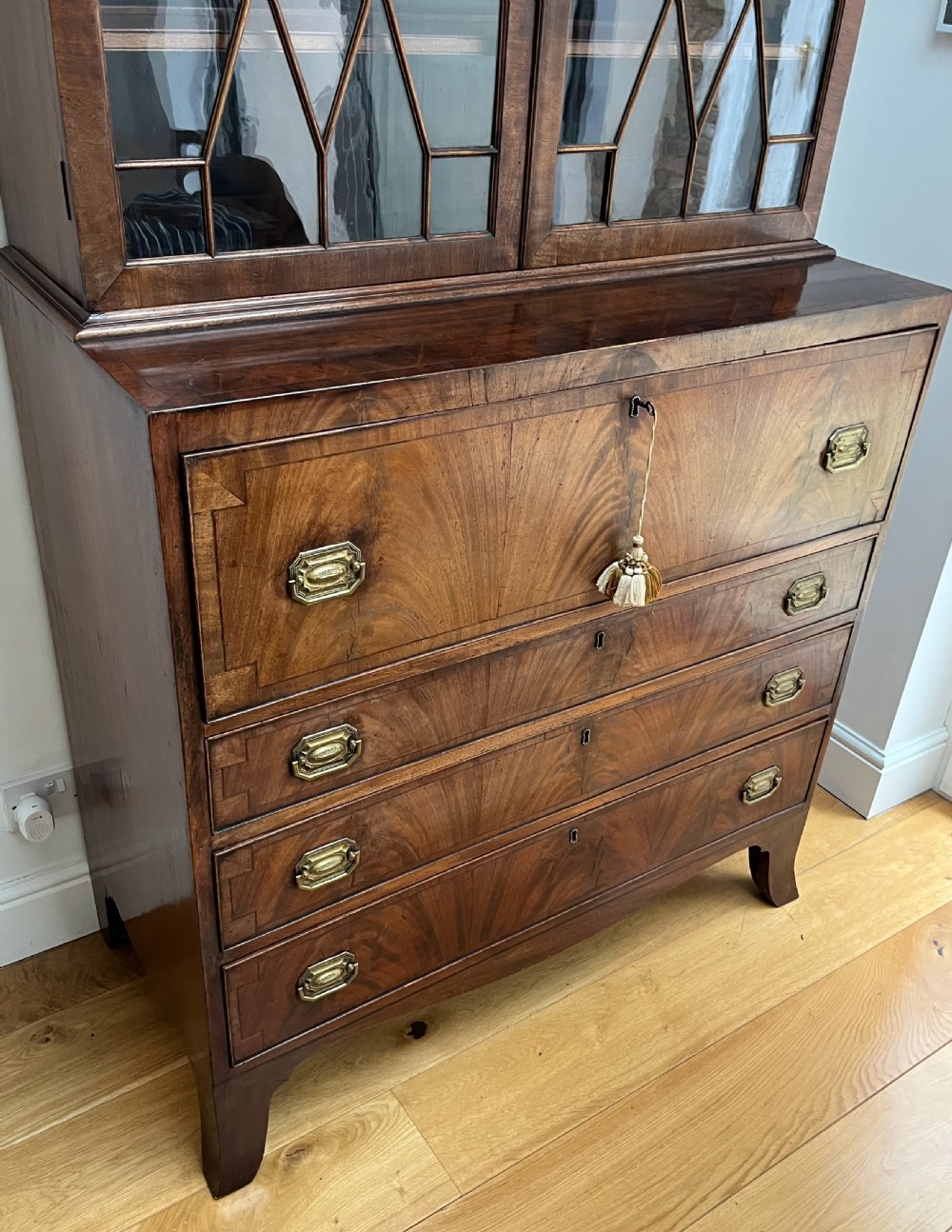 A Georgian mahogany secretaire bookcase featuring a double door upper cabinet with diamond astragal glazing, brass finials, and a lower chest of four drawers with brass drop handles. View III