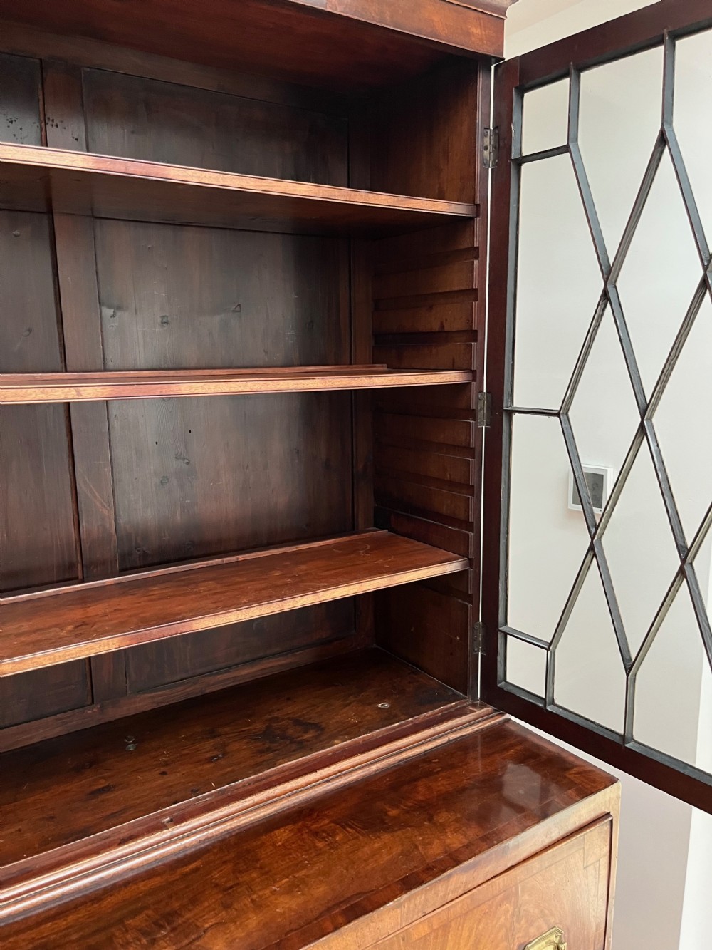 A Georgian mahogany secretaire bookcase featuring a double door upper cabinet with diamond astragal glazing, brass finials, and a lower chest of four drawers with brass drop handles. View VII