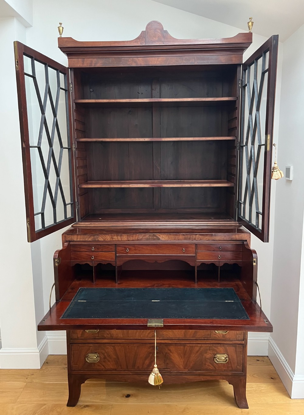 A Georgian mahogany secretaire bookcase featuring a double door upper cabinet with diamond astragal glazing, brass finials, and a lower chest of four drawers with brass drop handles. View VIII
