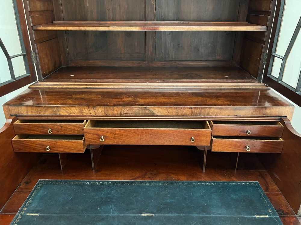 A Georgian mahogany secretaire bookcase featuring a double door upper cabinet with diamond astragal glazing, brass finials, and a lower chest of four drawers with brass drop handles. View X