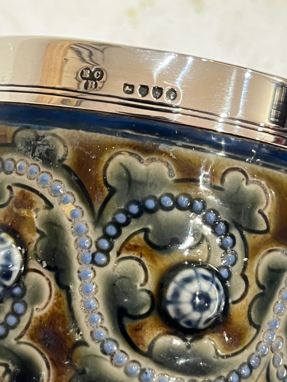 A Victorian Doulton Lambeth stoneware beaker featuring raised beaded scrollwork, floral motifs, and a hallmarked silver rim. View II