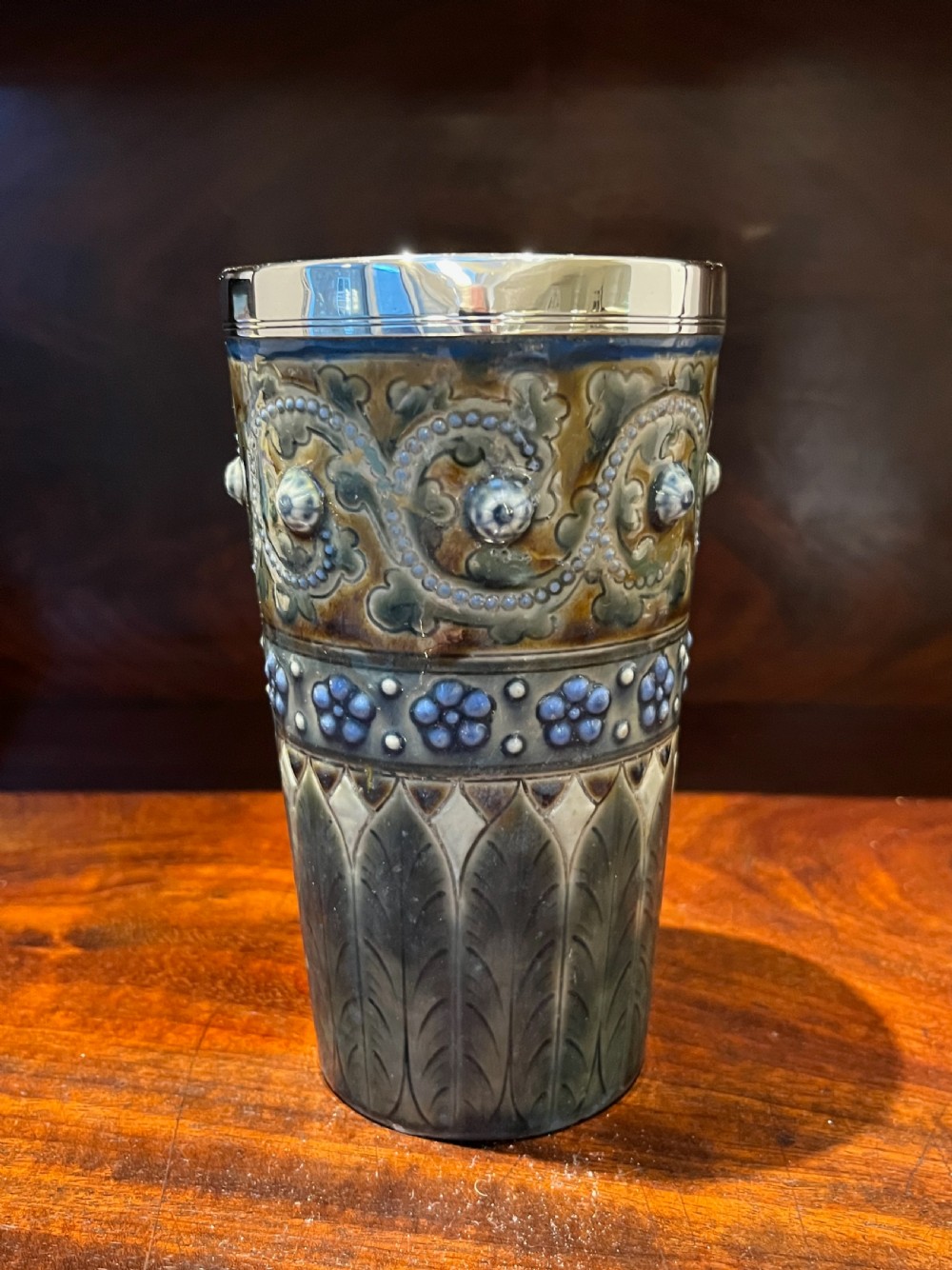 A Victorian Doulton Lambeth stoneware beaker featuring raised beaded scrollwork, floral motifs, and a hallmarked silver rim. View VII