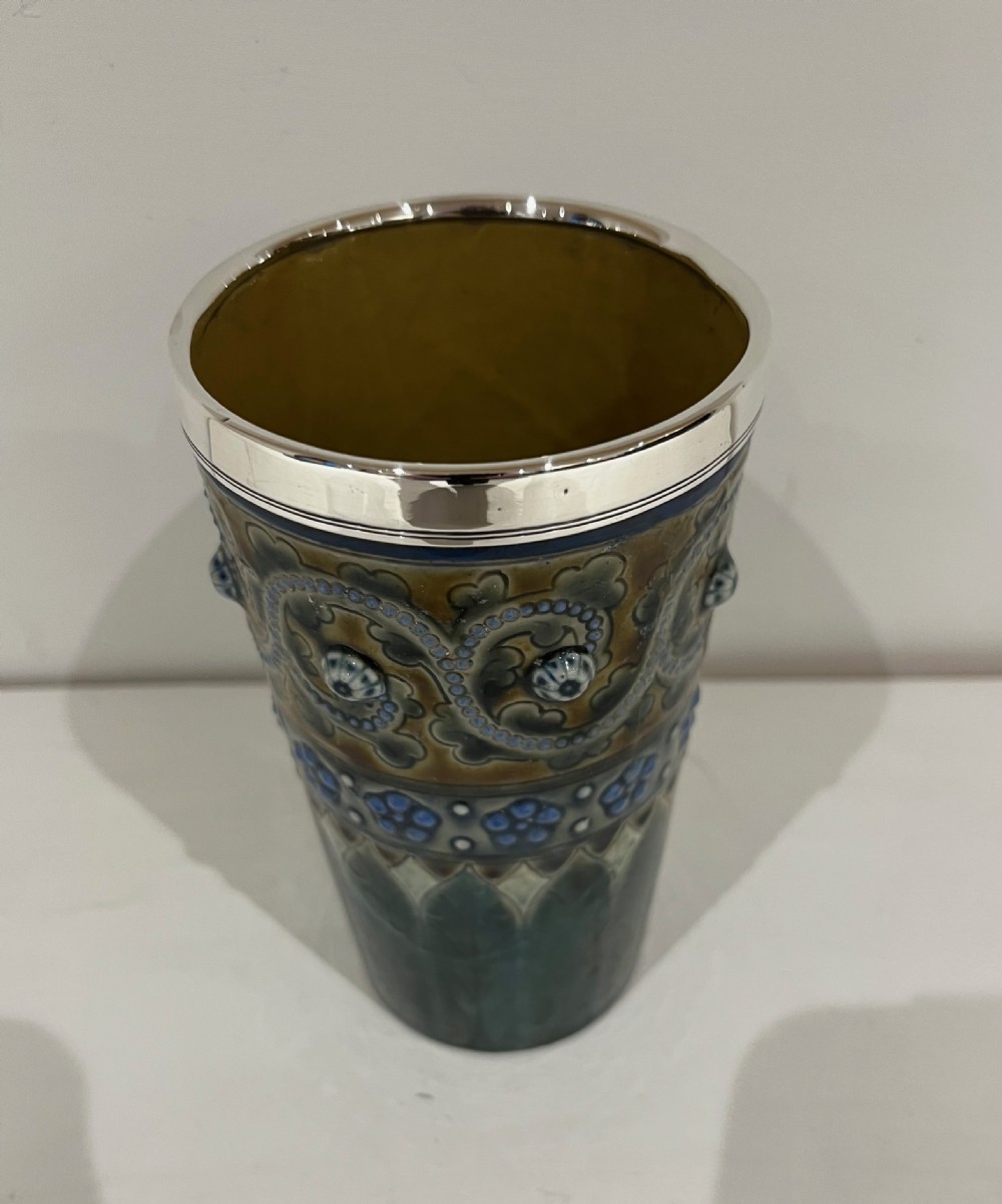 A Victorian Doulton Lambeth stoneware beaker featuring raised beaded scrollwork, floral motifs, and a hallmarked silver rim. View X