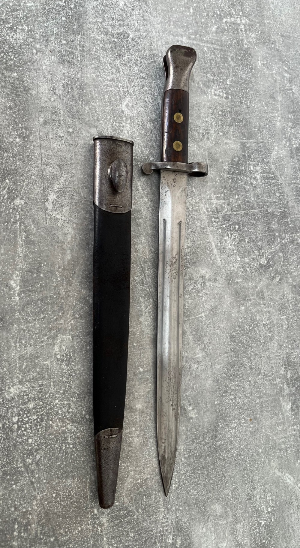A Victorian British Pattern 1888 Mark 1 Type 2 sword bayonet with a double-edged steel blade, wooden handle grips secured with brass rivets, alongside its dark leather and steel-mounted scabbard.