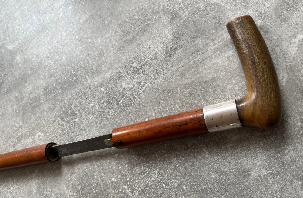 An antique Malacca wood walking stick unsheathed to reveal an etched steel Toledo blade alongside a silver collar and horn handle. View III