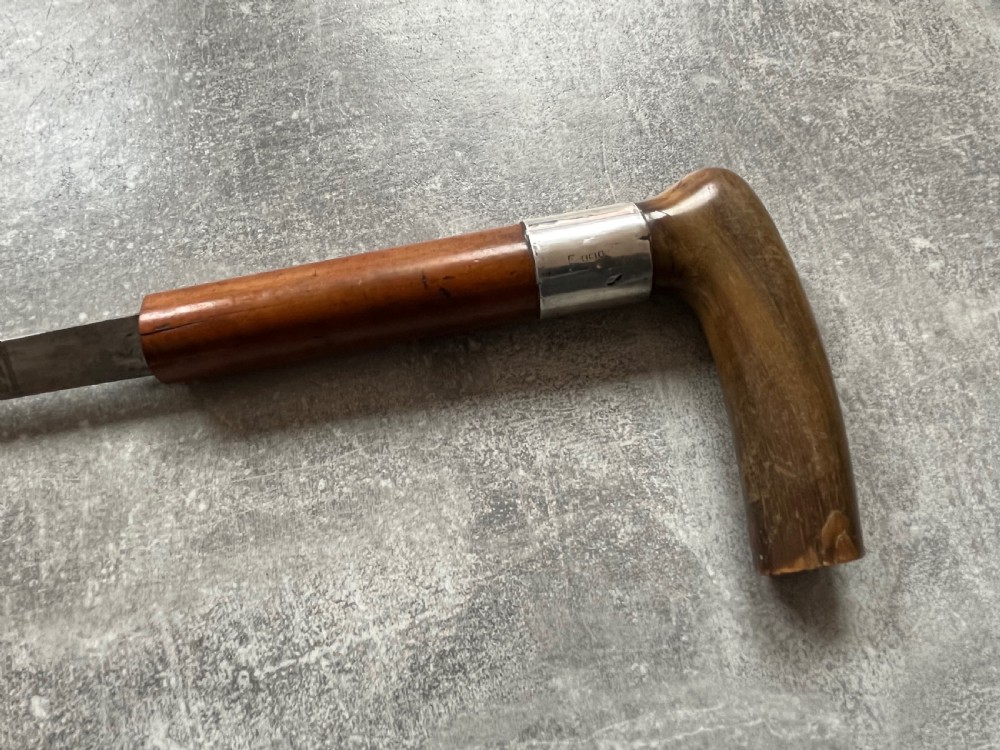 An antique Malacca wood walking stick unsheathed to reveal an etched steel Toledo blade alongside a silver collar and horn handle. View IX