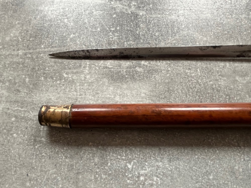 An antique Malacca wood walking stick unsheathed to reveal an etched steel Toledo blade alongside a silver collar and horn handle. View X
