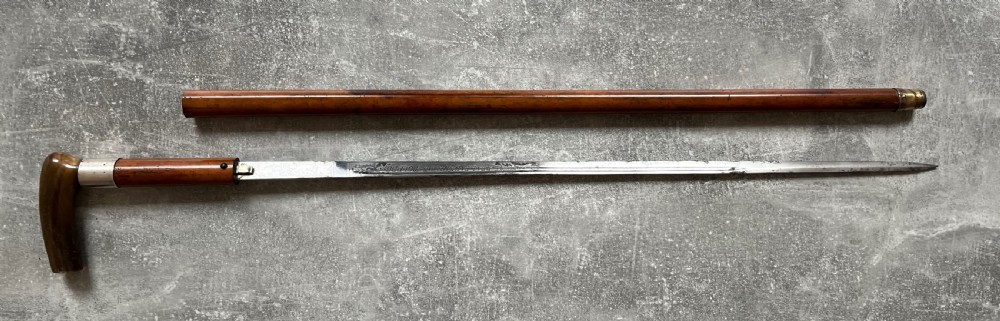 An antique Malacca wood walking stick unsheathed to reveal an etched steel Toledo blade alongside a silver collar and horn handle. View XIV