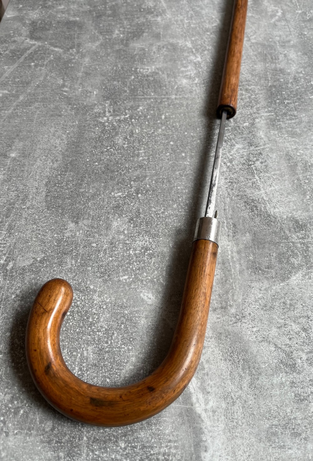 An antique crook-handled malacca walking cane unsheathed to reveal a long, slender steel sword blade beside its hollow wooden shaft. View III