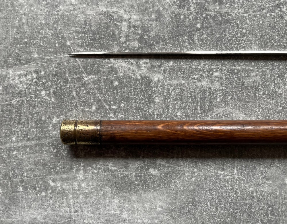 An antique crook-handled malacca walking cane unsheathed to reveal a long, slender steel sword blade beside its hollow wooden shaft. View VIII