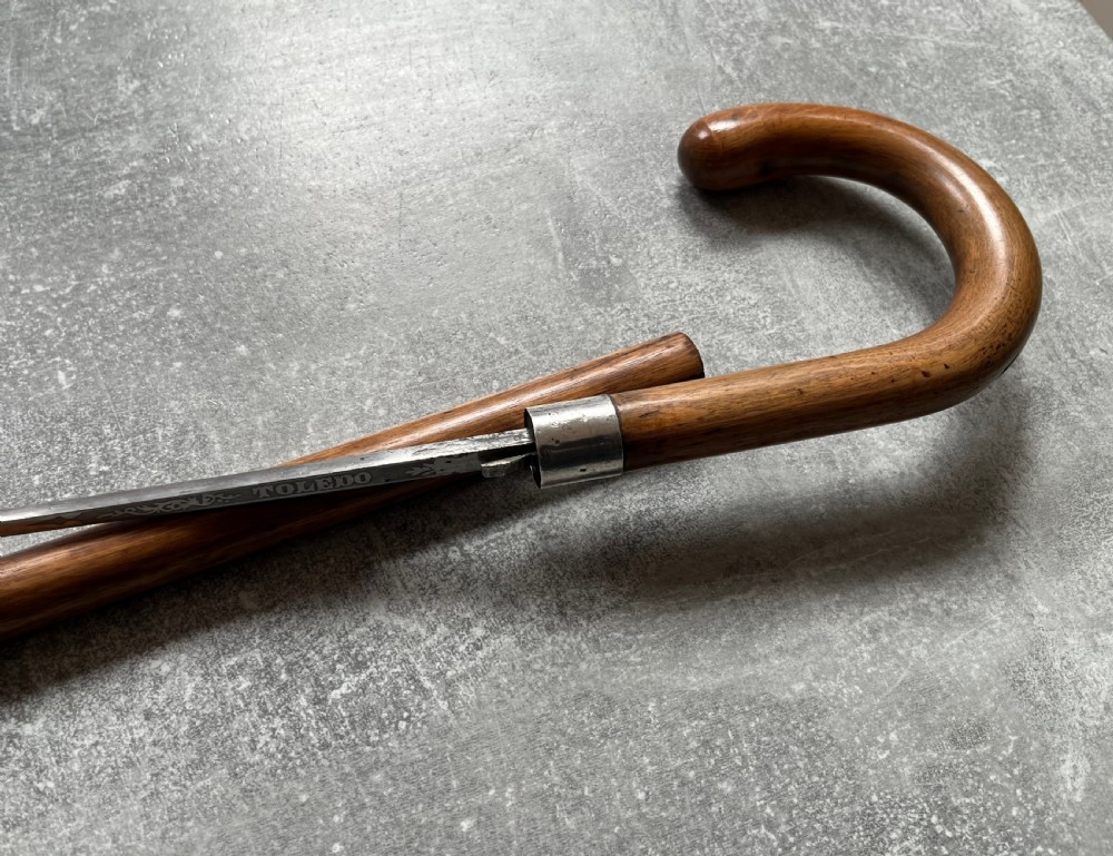 An antique crook-handled malacca walking cane unsheathed to reveal a long, slender steel sword blade beside its hollow wooden shaft. View X