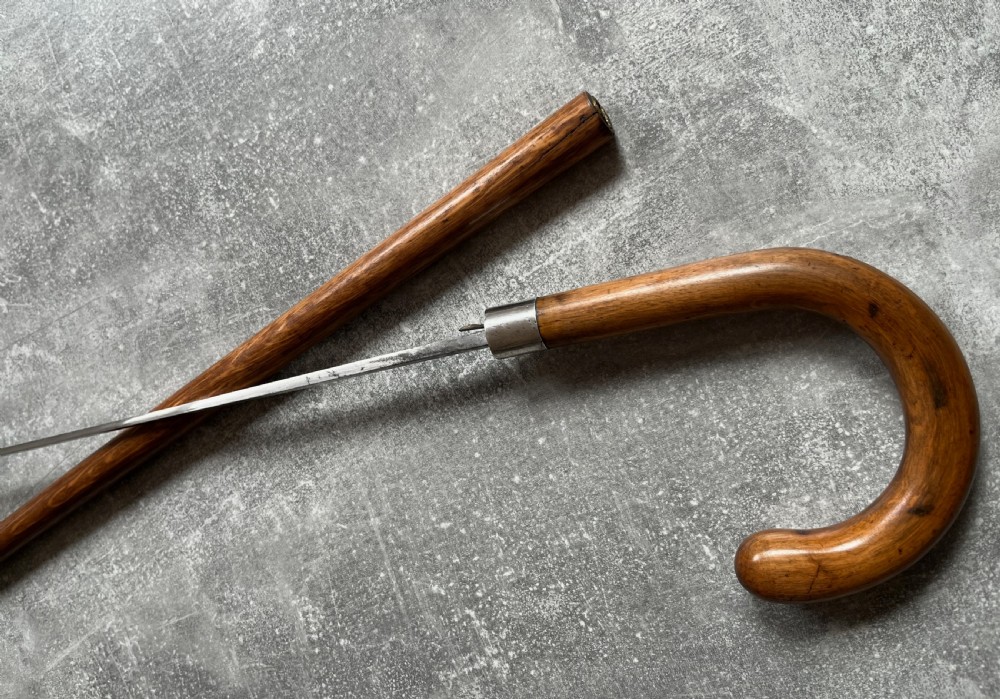 An antique crook-handled malacca walking cane unsheathed to reveal a long, slender steel sword blade beside its hollow wooden shaft. View XI