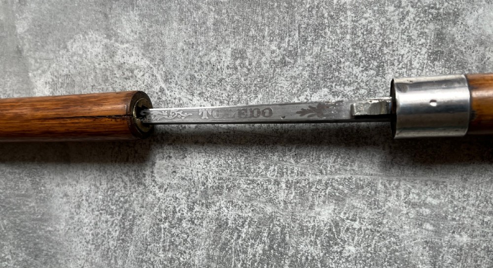 An antique crook-handled malacca walking cane unsheathed to reveal a long, slender steel sword blade beside its hollow wooden shaft. View XII