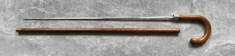 An antique crook-handled malacca walking cane unsheathed to reveal a long, slender steel sword blade beside its hollow wooden shaft. View XIV