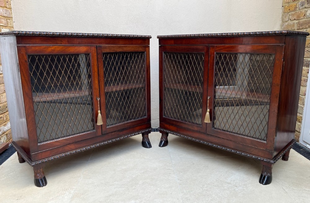 A pair of antique Regency mahogany side cabinets featuring brass lattice glazed doors and carved cloven hoof feet.