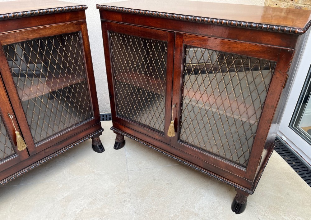 A pair of antique Regency mahogany side cabinets featuring brass lattice glazed doors and carved cloven hoof feet. View II