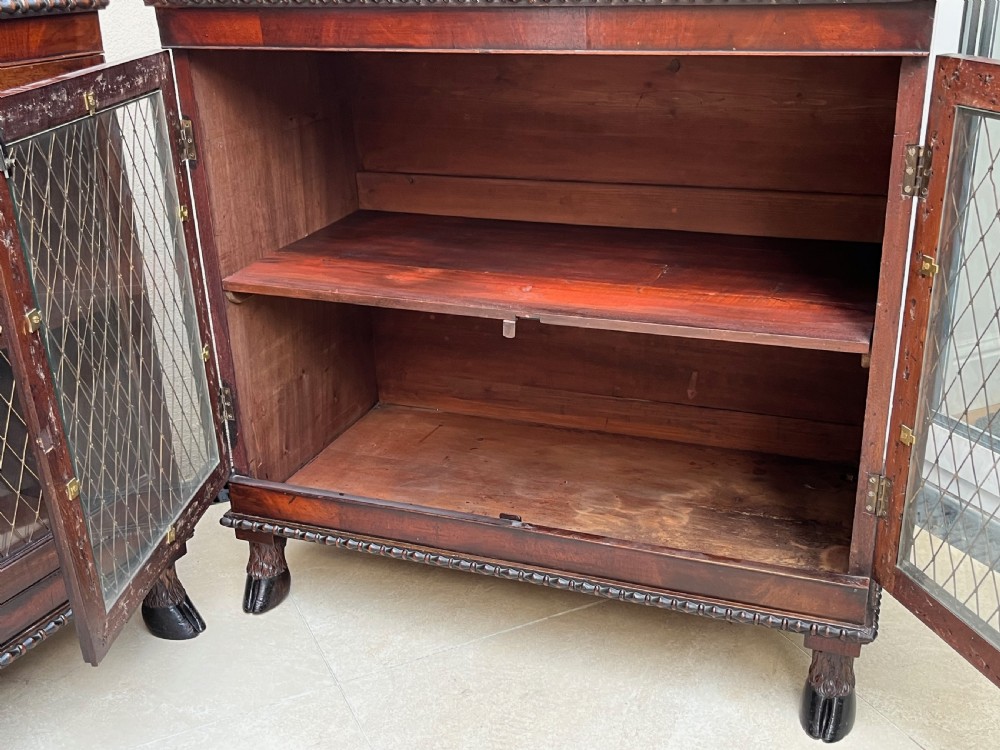A pair of antique Regency mahogany side cabinets featuring brass lattice glazed doors and carved cloven hoof feet. View IX