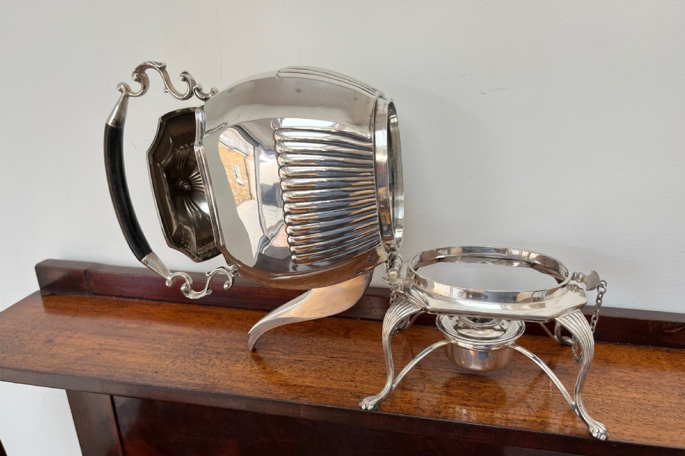 A silver-plated spirit kettle with a fluted lower body, dark wooden handle, gooseneck spout, and matching stand containing an alcohol burner below. View IV