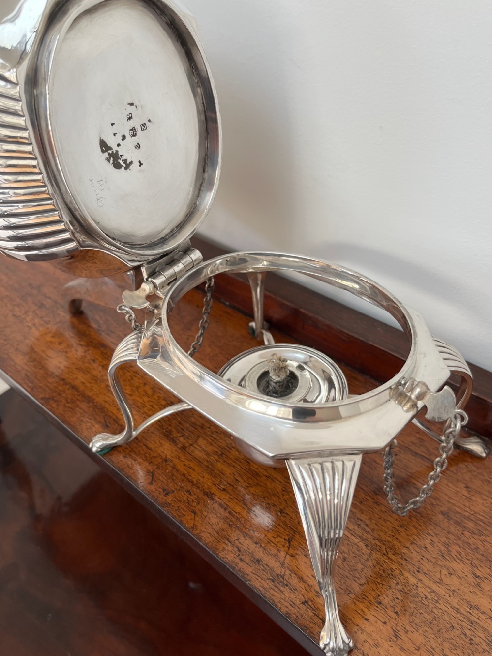A silver-plated spirit kettle with a fluted lower body, dark wooden handle, gooseneck spout, and matching stand containing an alcohol burner below. View VI