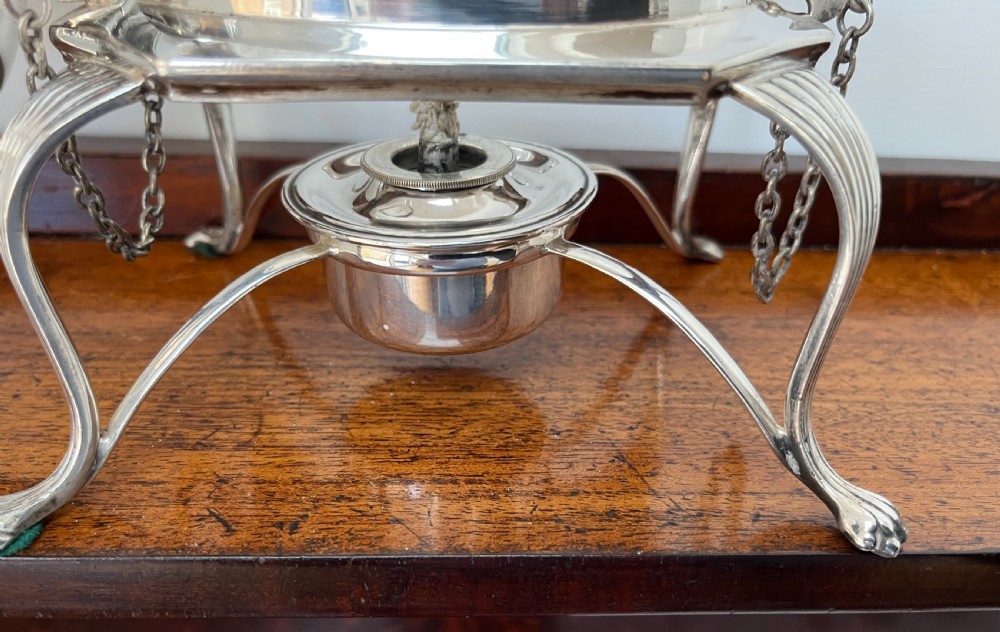 A silver-plated spirit kettle with a fluted lower body, dark wooden handle, gooseneck spout, and matching stand containing an alcohol burner below. View VII