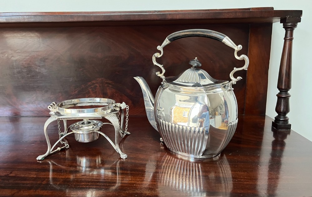 A silver-plated spirit kettle with a fluted lower body, dark wooden handle, gooseneck spout, and matching stand containing an alcohol burner below. View VIII